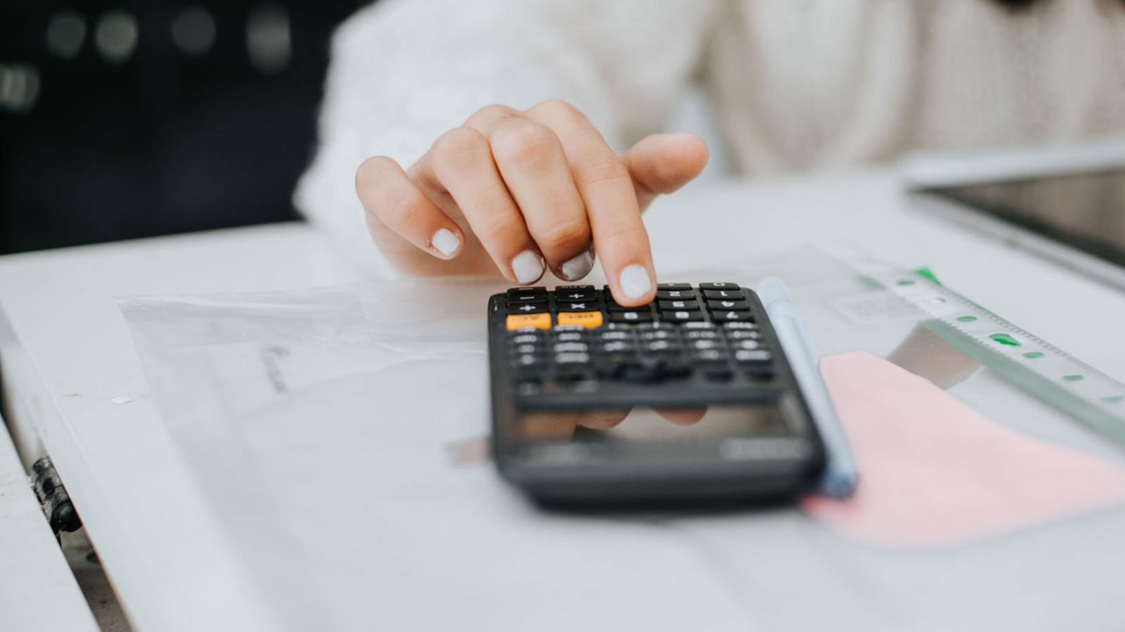 Calculator laying on top of paper with hand typing in numbers.